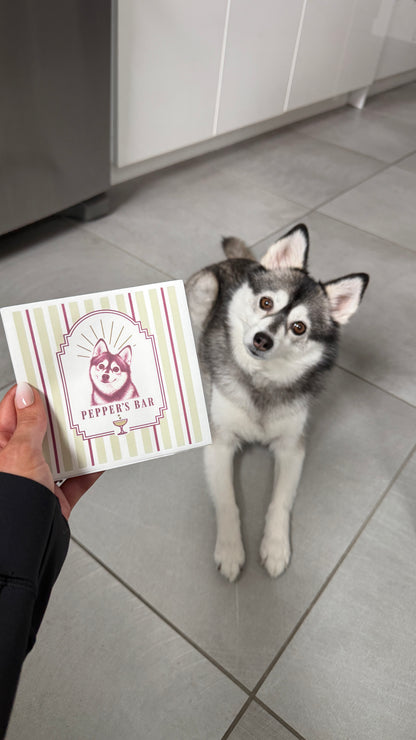 Personalized dog portrait cocktail napkin with a striped border held next to a husky dog