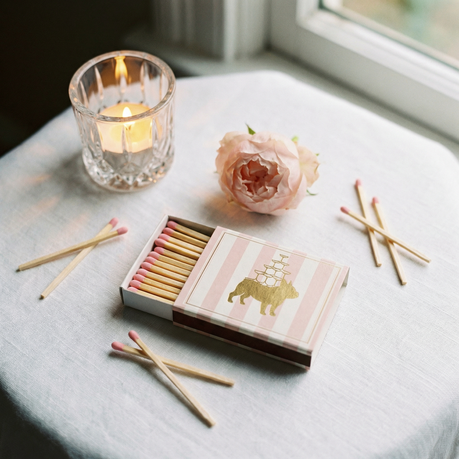 Matchbox with matches, lit candle, and pink flower on a light surface
