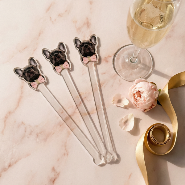 Set of four dog-shaped cocktail stirrers on a marble surface with a glass of champagne and a flower.