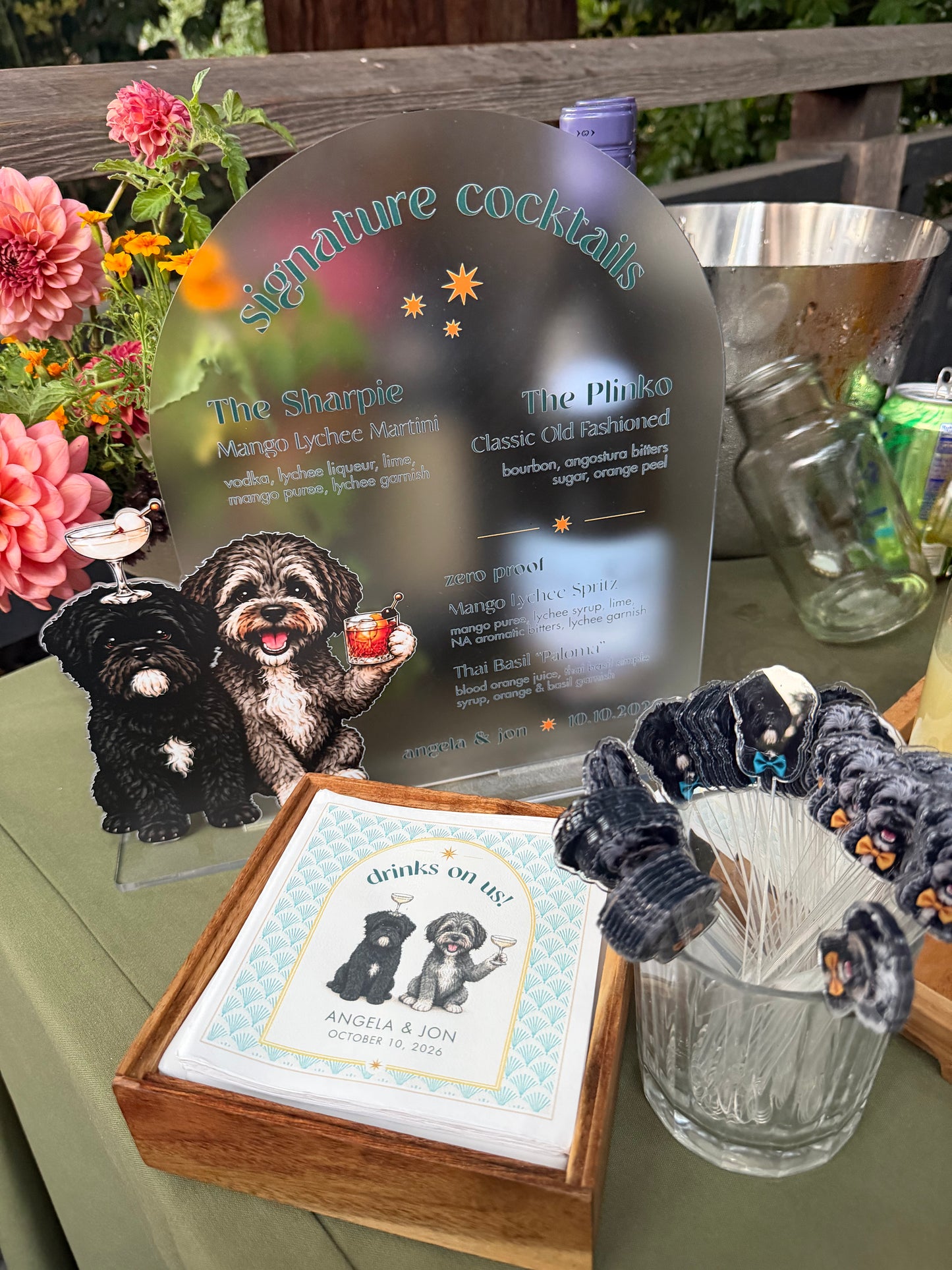 Wedding signature cocktail bar with an acrylic menu sign, dog stirrers, custom napkins and flowers