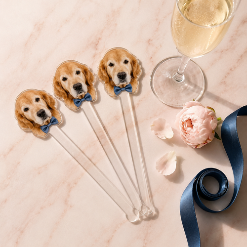 Dog-themed cocktail stirrers with a glass of champagne and flowers on a marble surface