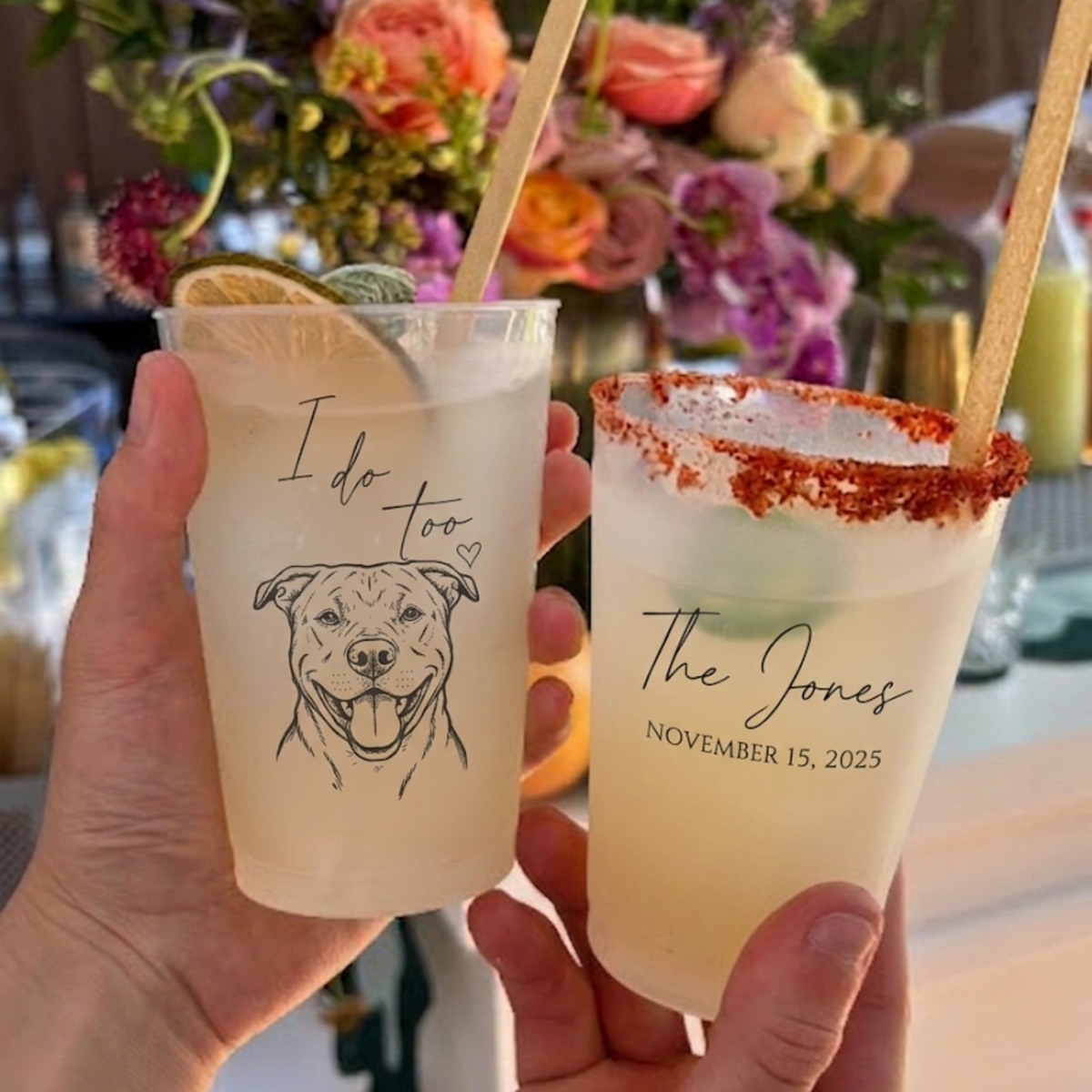 Two personalized drinks held by a hand with floral decorations in the background