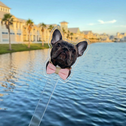 Dog-shaped balloon with a dog wearing a pink bow tie over a waterfront with buildings in the background
